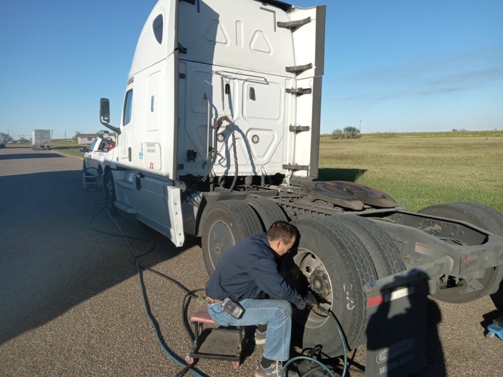 Technician working a wheel end beside a white sleeper tractor at the roadside
